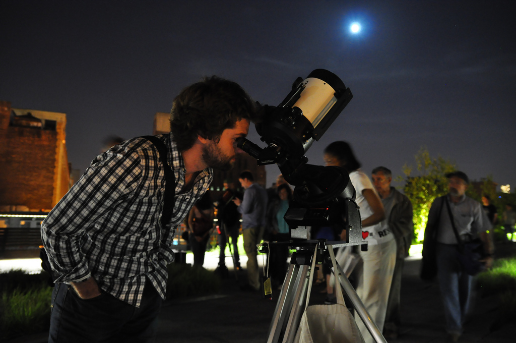 People taking turns viewing through a telescope pointed at the night sky.