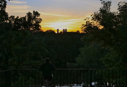 Photo of girl leaning against railing watching sunset over downtown Minneapolis from The Monument.