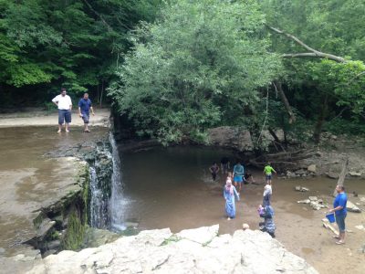 Families play at the bottom of the waterfall while two men look at the view from on top of it in Nerstrand Big Woods State Park.