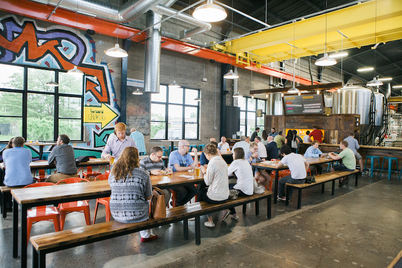 People sitting at picnic table style seating inside a colorful brewery drinking beer.