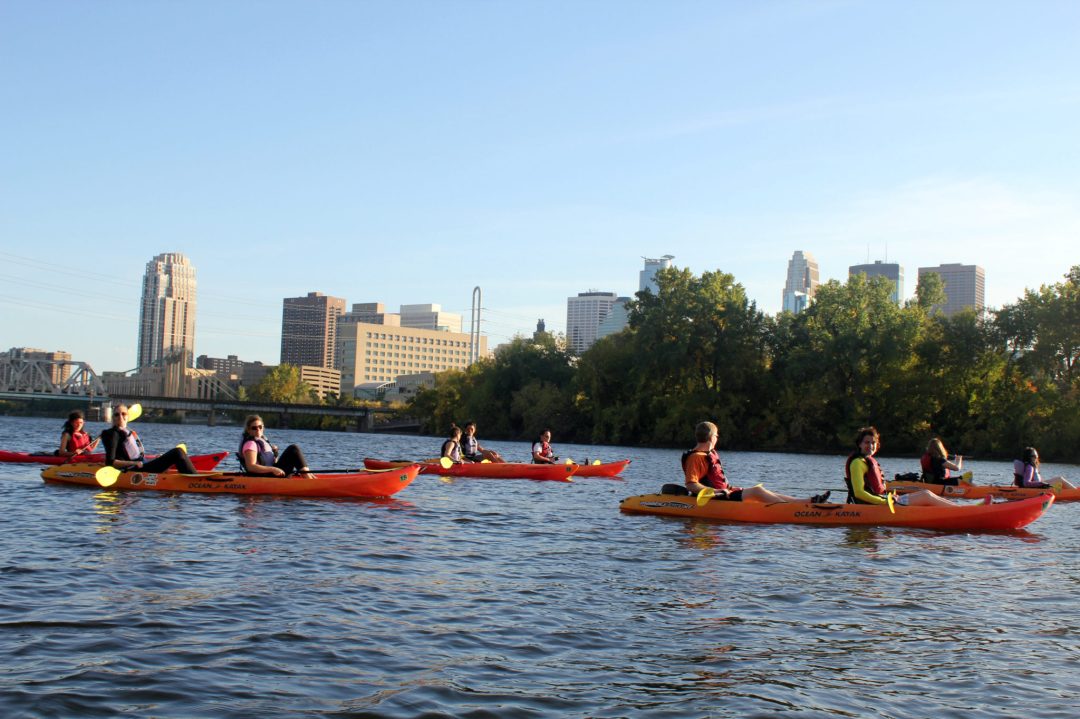 A group of kayakers out for a morning stroll on the Mississippi River. In the background is the Minneapolis skyline.