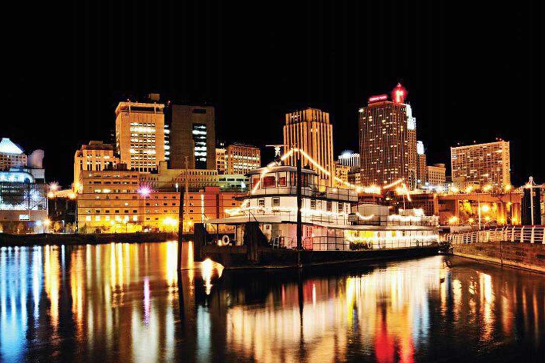 The Covington Inn Bed and Breakfast floats in the waters of the Mississippi River at night with the St. Paul skyline lighting up the background.